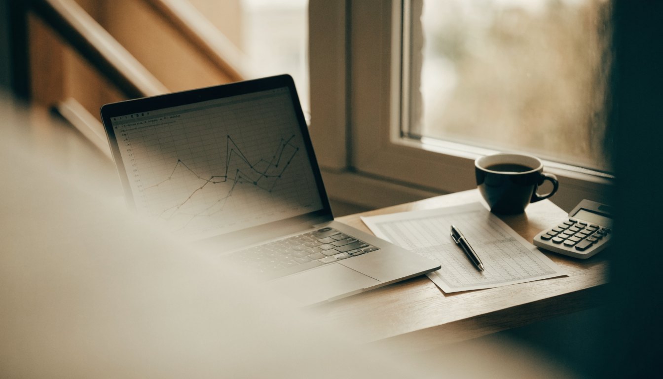 Desk with a laptop showing a market chart, printed figures and a calculator, illustrating home valuation analysis