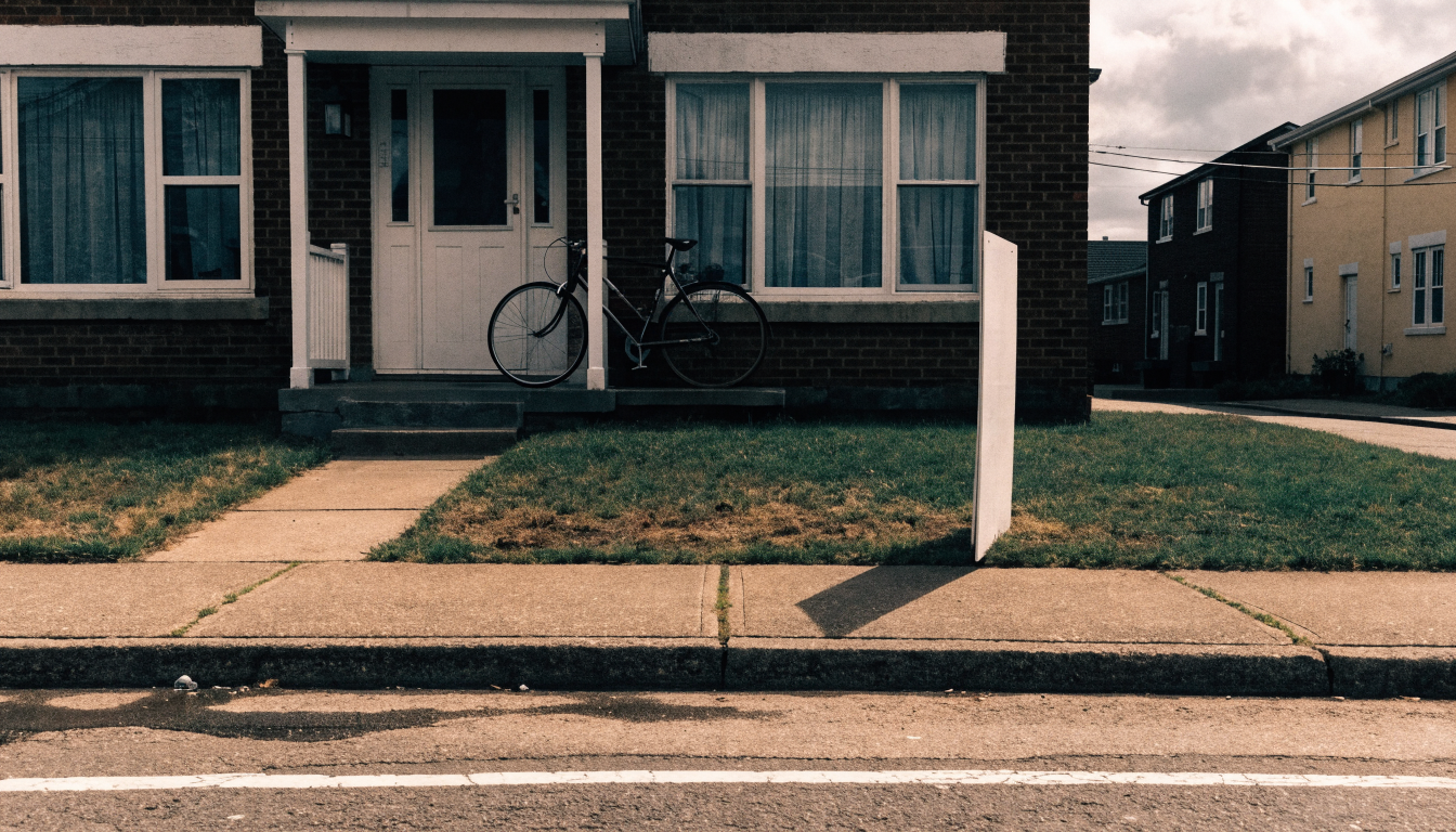 A for-sale sign on the lawn of a lived-in Toronto semi-detached house, curtains drawn and a bicycle on the porch