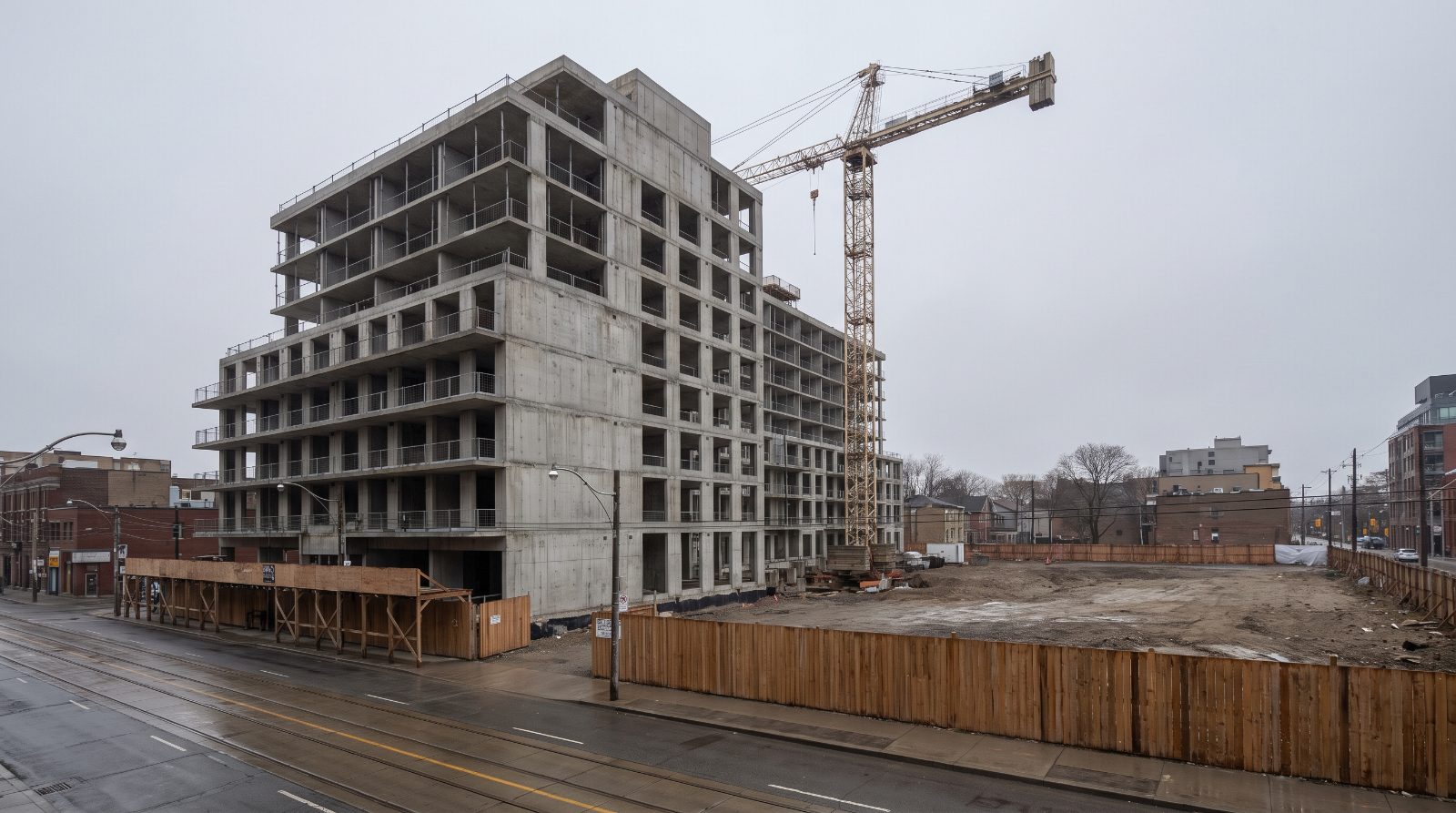 A stalled condominium construction site in Toronto — a completed concrete structure with no glazing, an idle crane and an empty lot, illustrating a paused new-build market