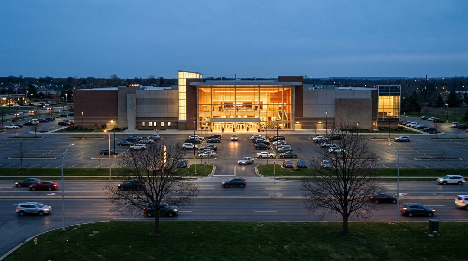 A large suburban cinema multiplex at dusk with an illuminated glass entrance and a wide parking lot