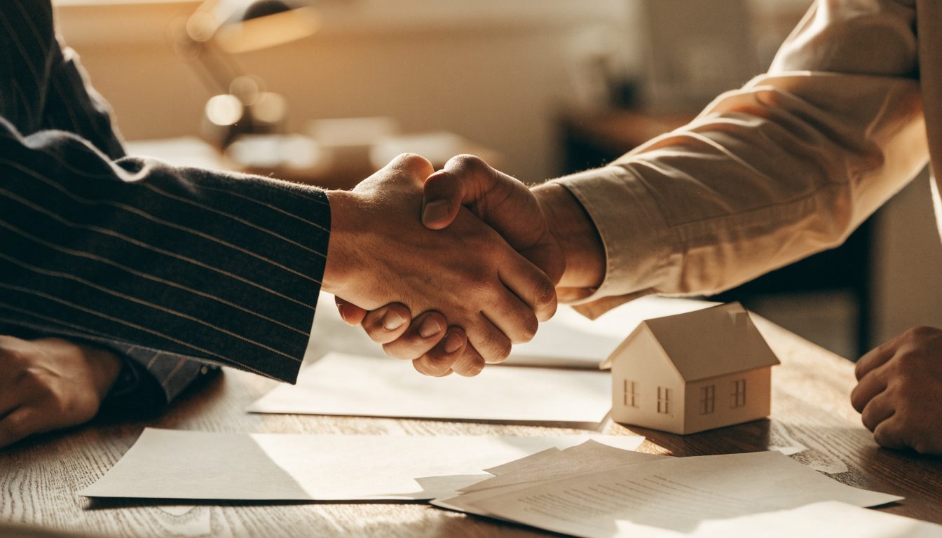 Handshake over paperwork and a small house model (illustrative)