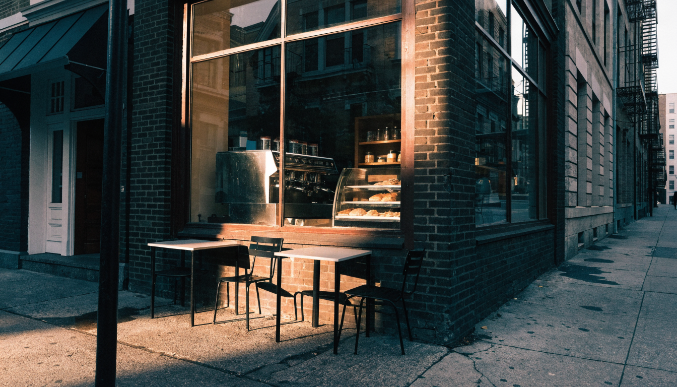 An independent neighbourhood coffee shop storefront in Etobicoke with a pastry case in the window and small tables on the pavement