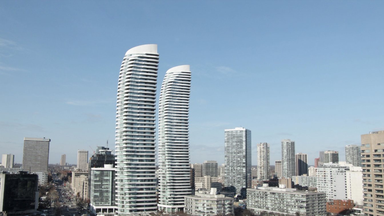 Two curving, twisting residential towers with continuous white balconies against a clear sky (illustrative)