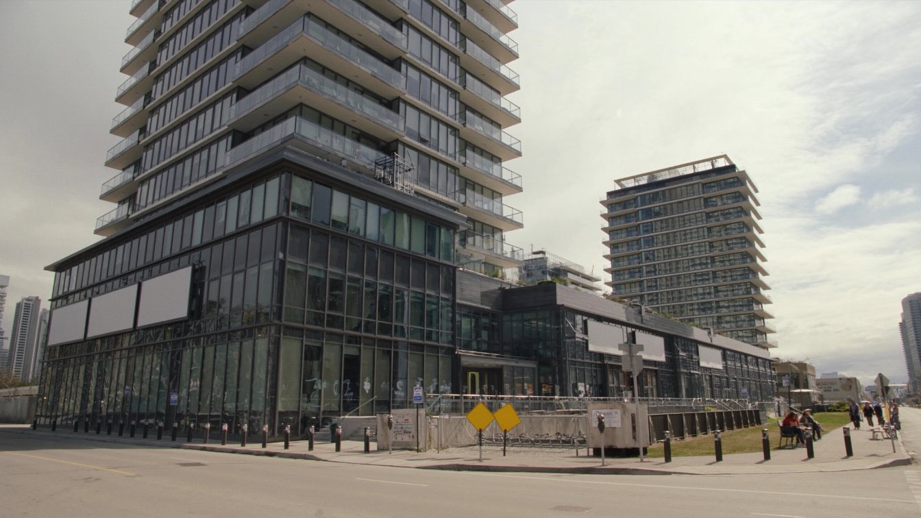 Newly completed tall glass residential tower with a grocery store at its base on a wide suburban-downtown street (illustrative)