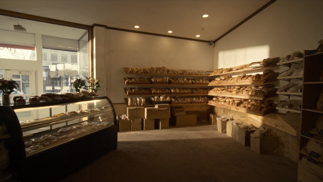 Neighbourhood bakery counter with bread racks and pastry display case, early morning light (illustrative)