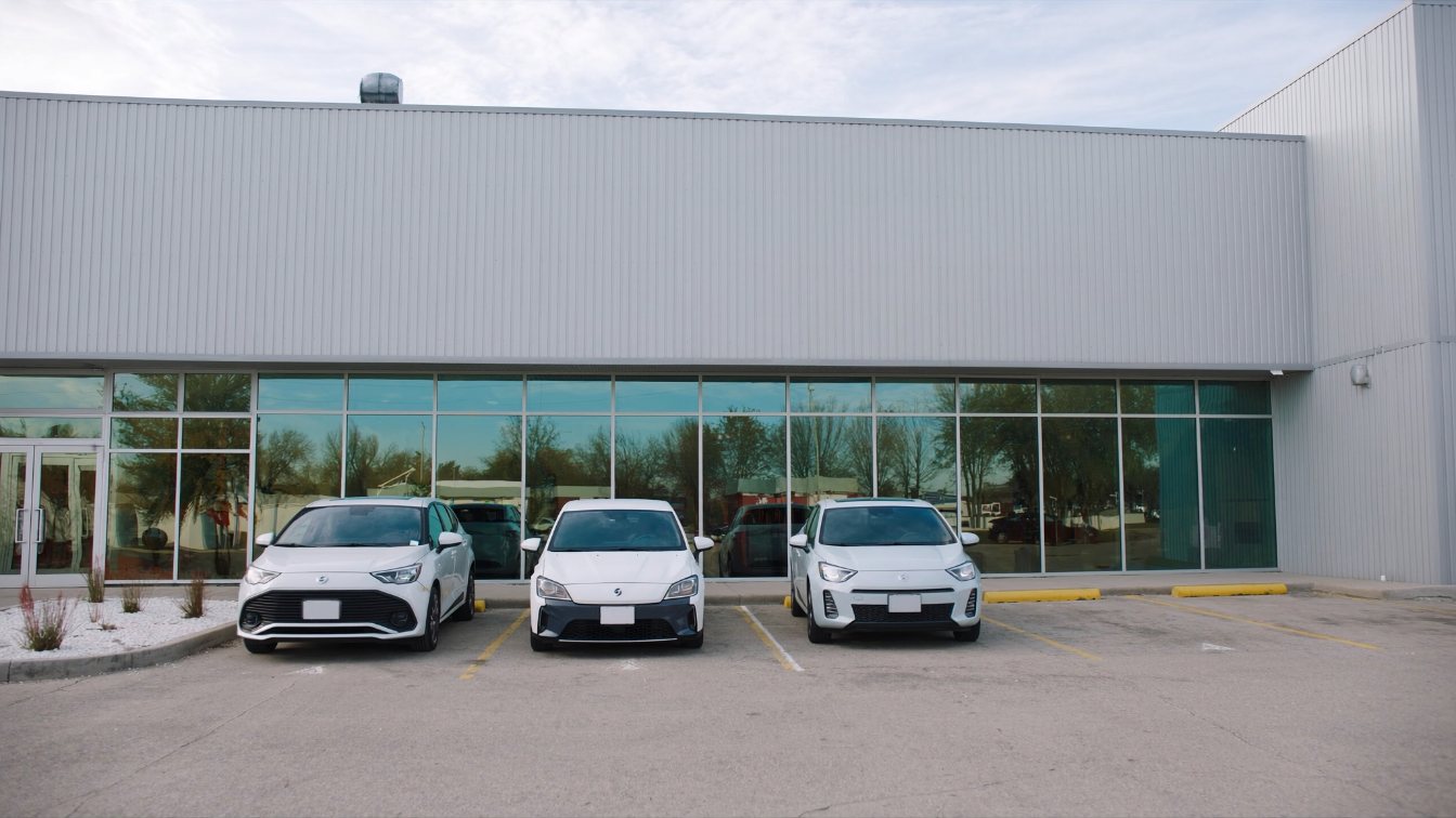 Row of compact driving school cars parked outside a small plaza office (illustrative)