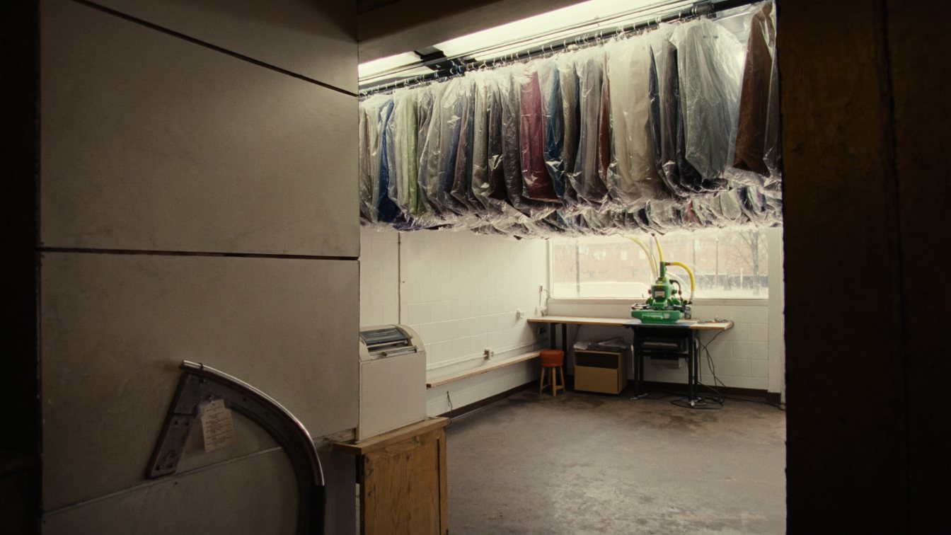 Garment conveyor and pressing equipment inside a small dry cleaning plant behind a storefront counter (illustrative)