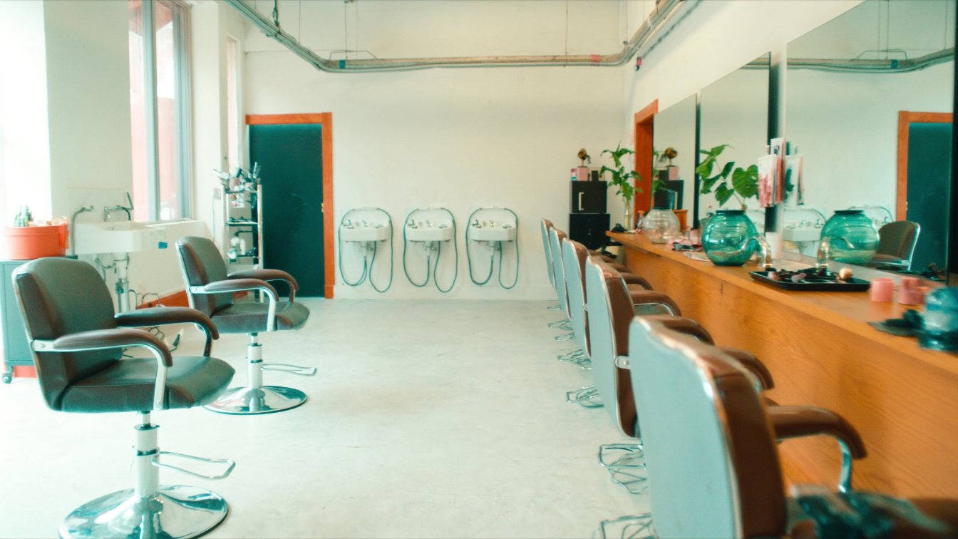 Row of styling chairs and mirrors in a bright neighbourhood hair salon with no clients (illustrative)