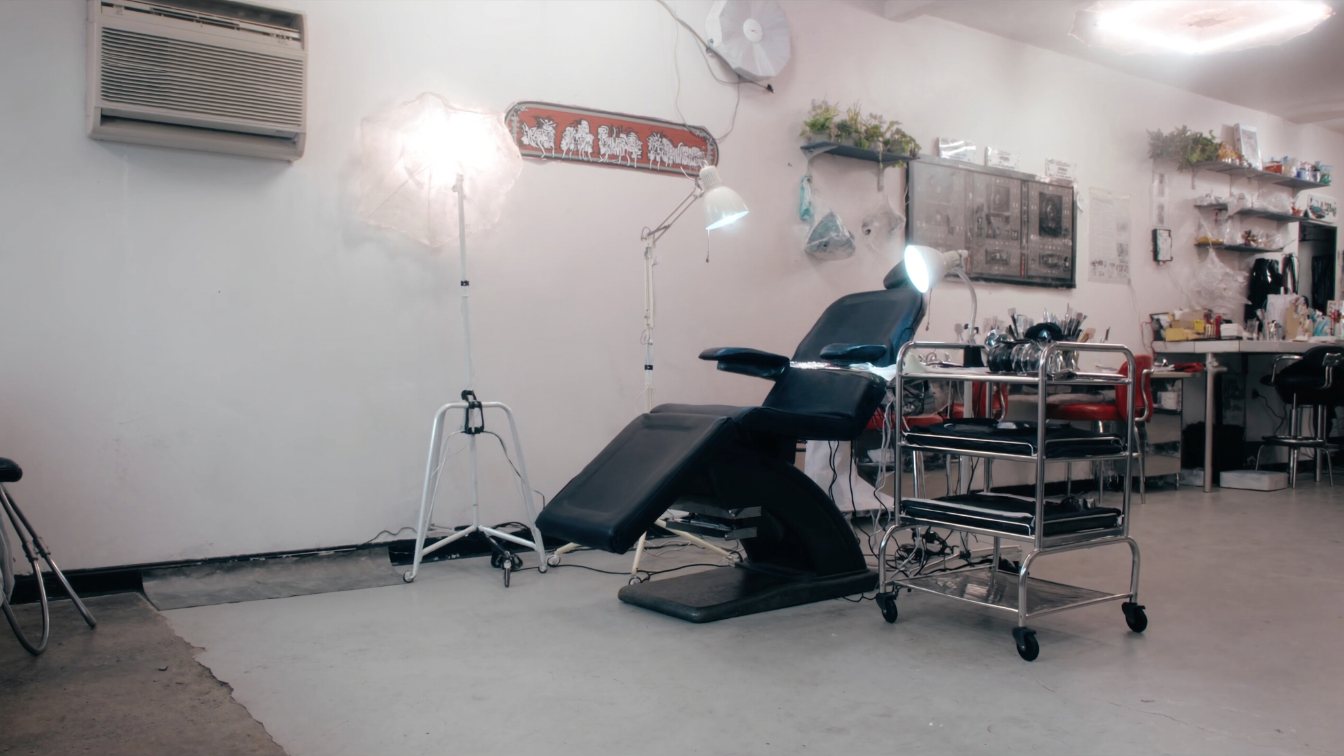 Clean tattoo studio workstation with a reclining client chair, stainless trolley and bright task lighting, no people (illustrative)