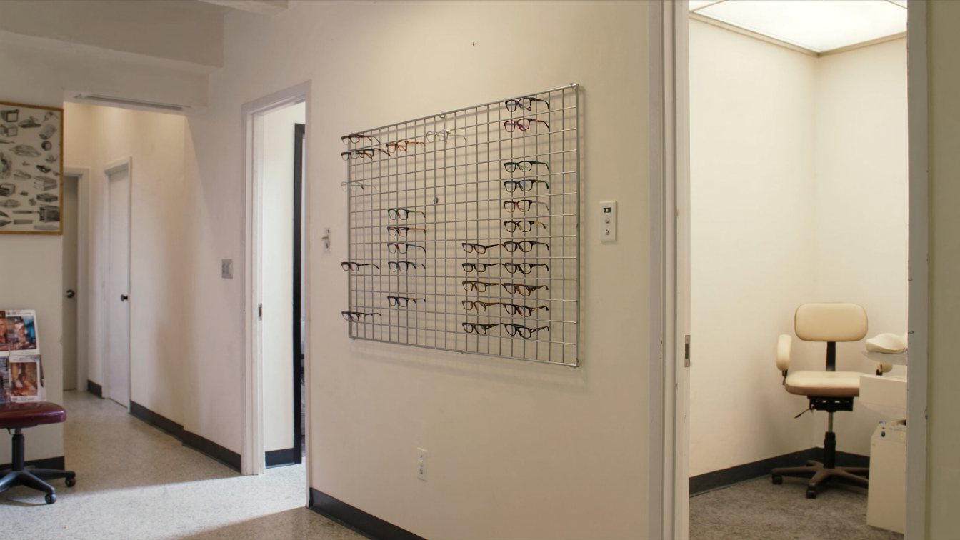 Bright optometry clinic reception with eyeglass frame displays and an exam room door in an Ontario plaza (illustrative)