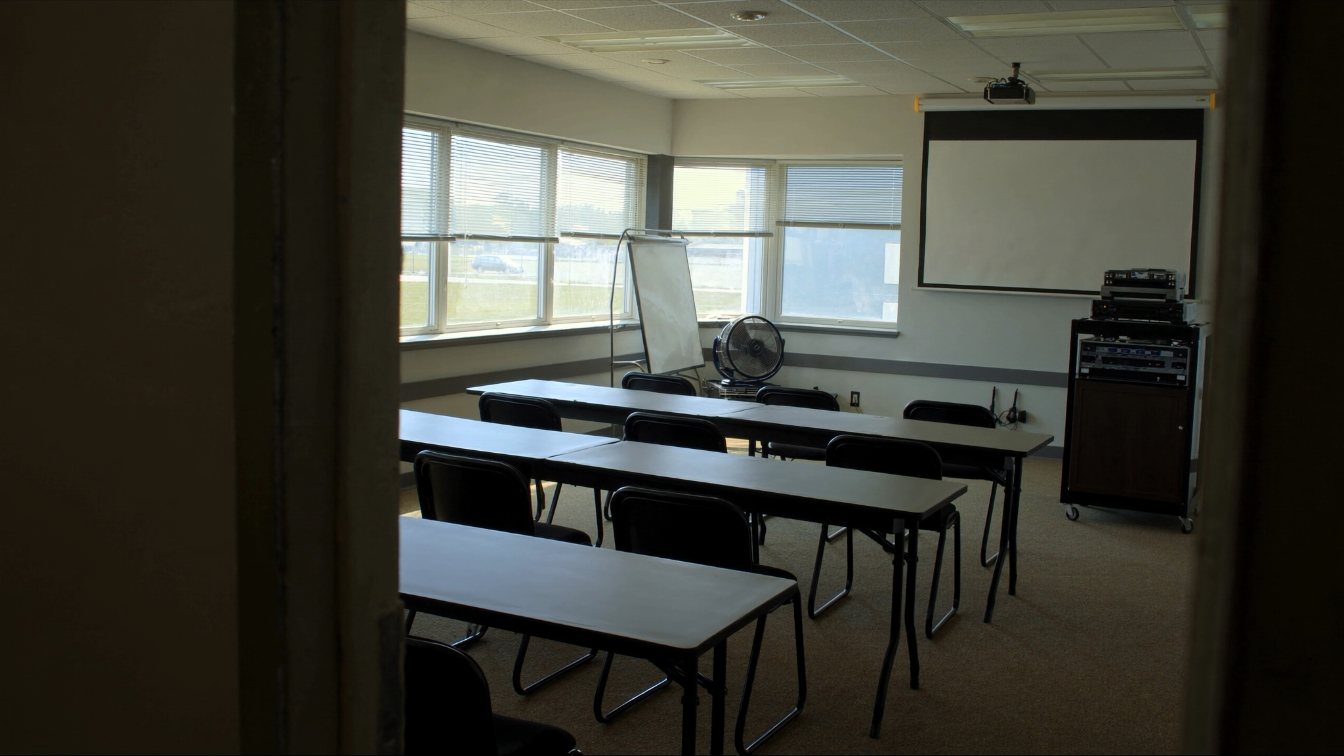 Small classroom with tables, chairs and a projector screen in a suburban office unit (illustrative)