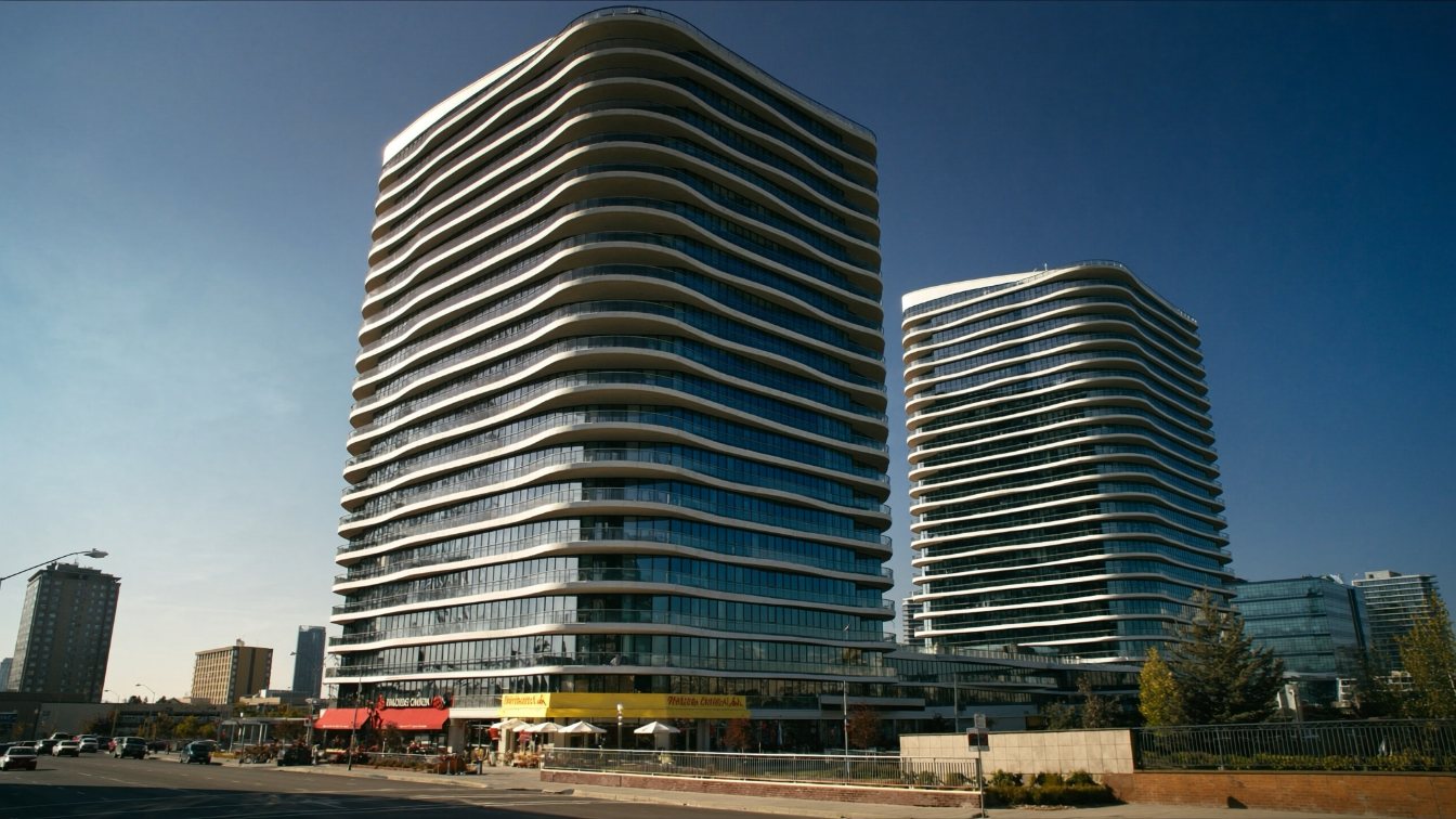 Two matching mid-height condominium towers with wave-patterned balconies on a wide suburban highway corridor (illustrative)
