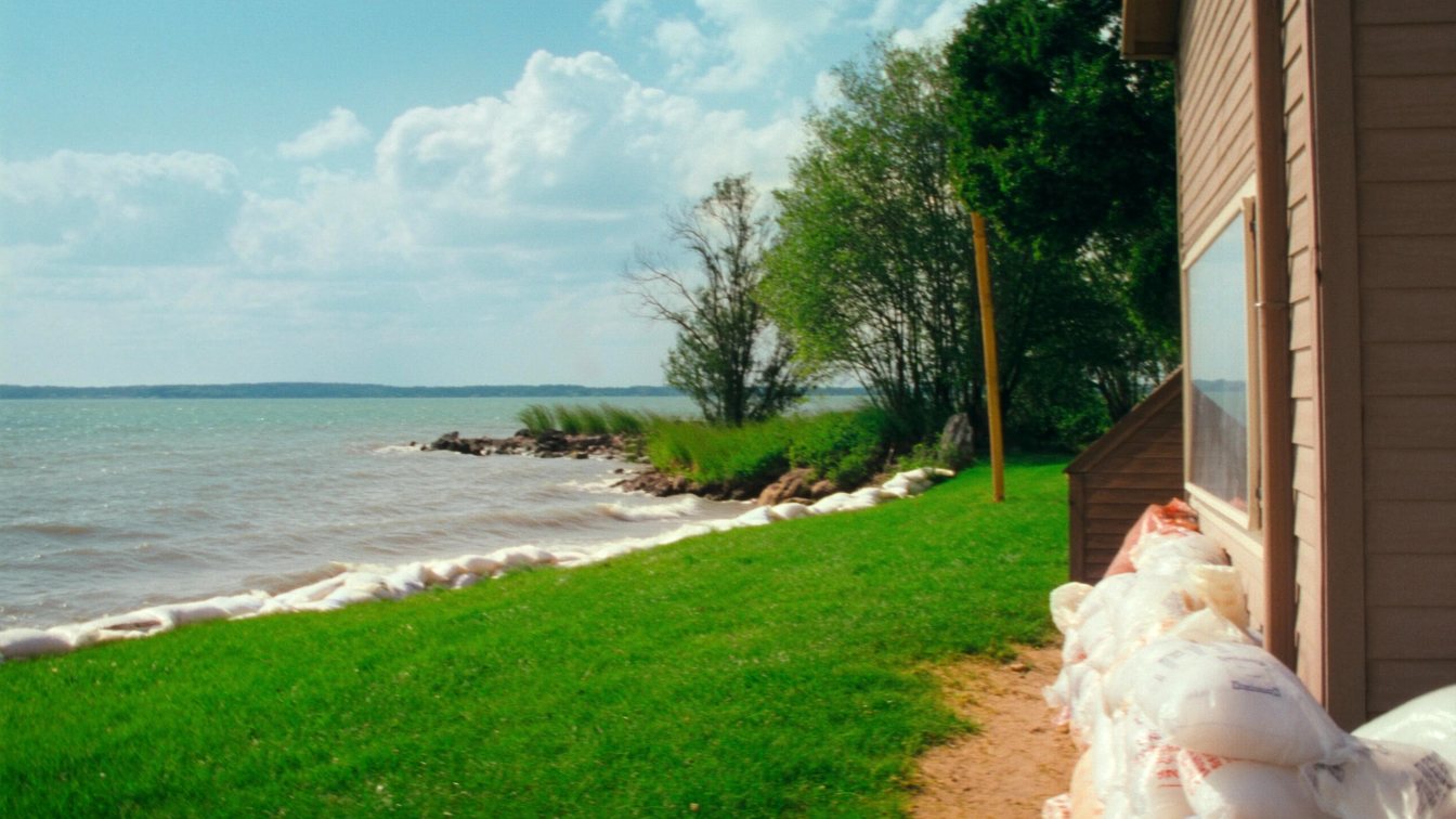 Lakefront home seen from the water during high lake levels with waves against a stone wall (illustrative)