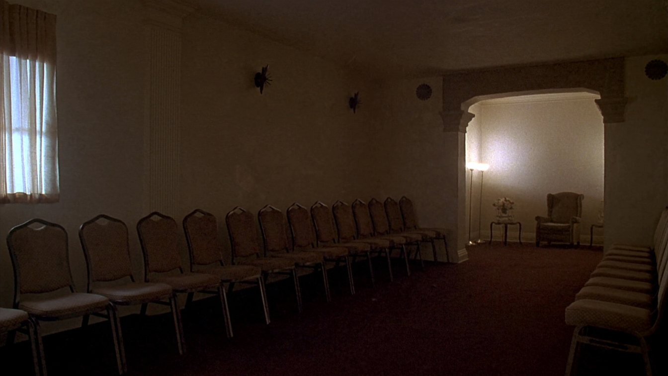 Quiet visitation room with rows of chairs and soft lighting inside a funeral home (illustrative)