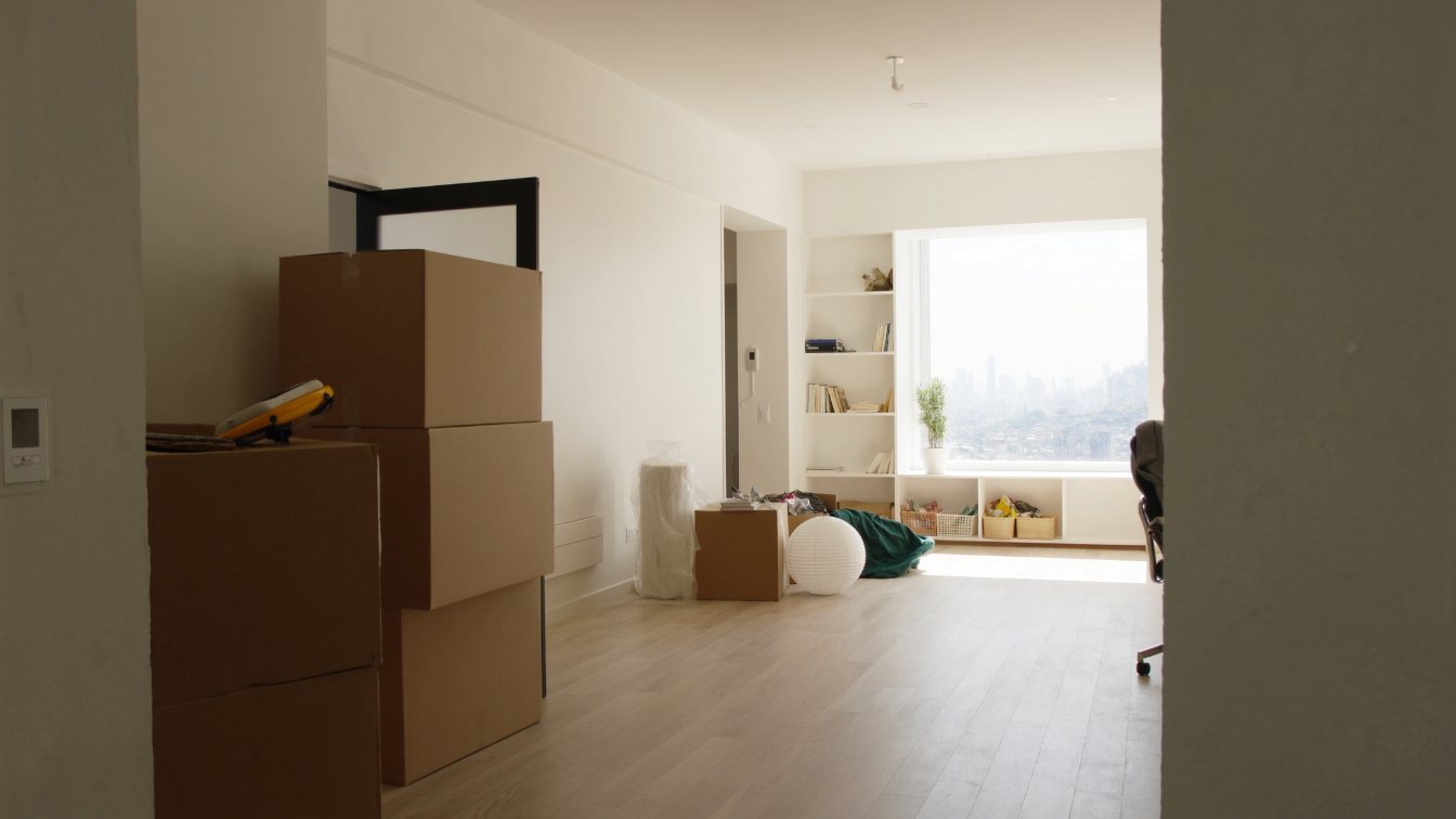 Bright condominium living room with boxes packed by the door, suggesting a tenant move (illustrative)