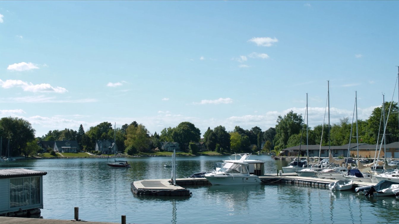 Boats moored along a Lake Simcoe shoreline with treed lots and a marina in the distance in Innisfil (illustrative)