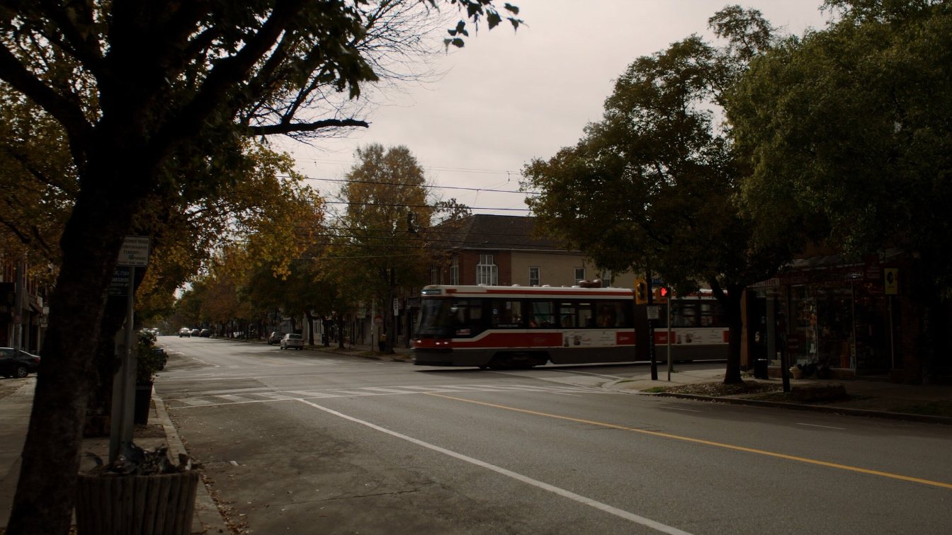 Toronto streetcar passing low-rise shops on a tree-lined street in autumn (illustrative)