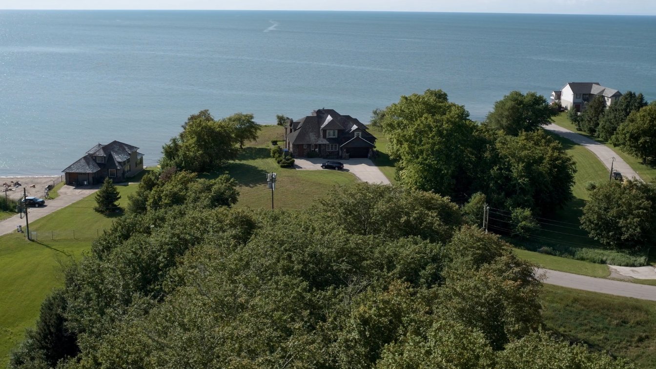 Three rows of homes stepping back from a Lake Ontario shoreline: on the water, across the street, and on the hill behind (illustrative)