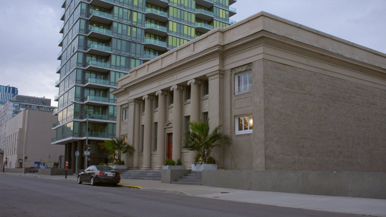 A tall glass condominium tower rising behind a restored early-1900s stone bank building on a downtown Toronto street (illustrative)