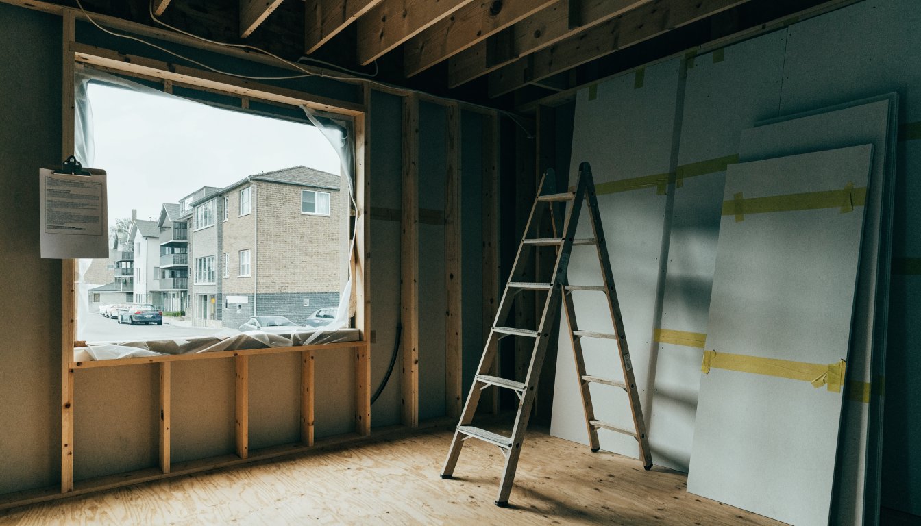 A gutted low-rise apartment unit mid-renovation, bare studs and plastic sheeting over the window, illustrating an Ontario N13 notice for repairs requiring vacant possession.