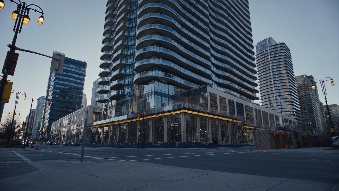 A very tall curved glass condominium tower on a retail podium at a busy downtown Toronto intersection (illustrative)