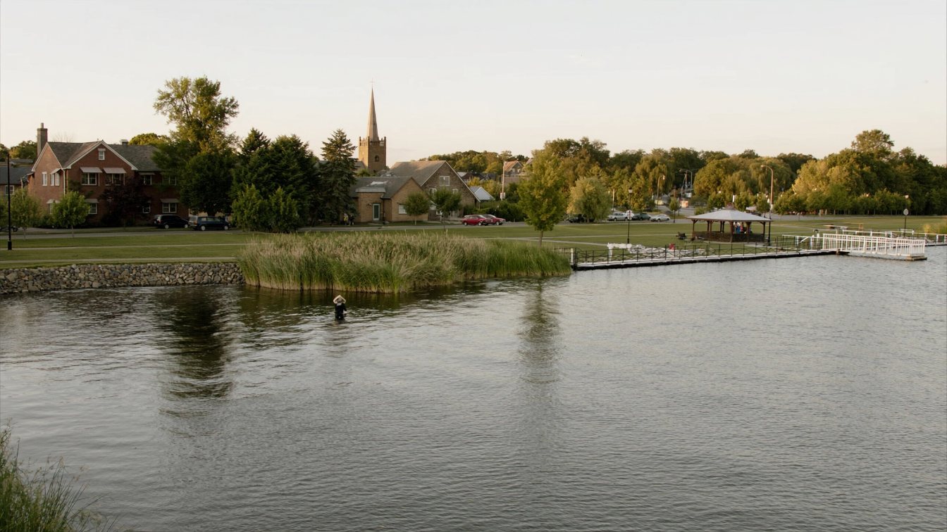 Wide, shallow lake with reeds along the shore and a small-town waterfront park in the distance near Port Perry (illustrative)