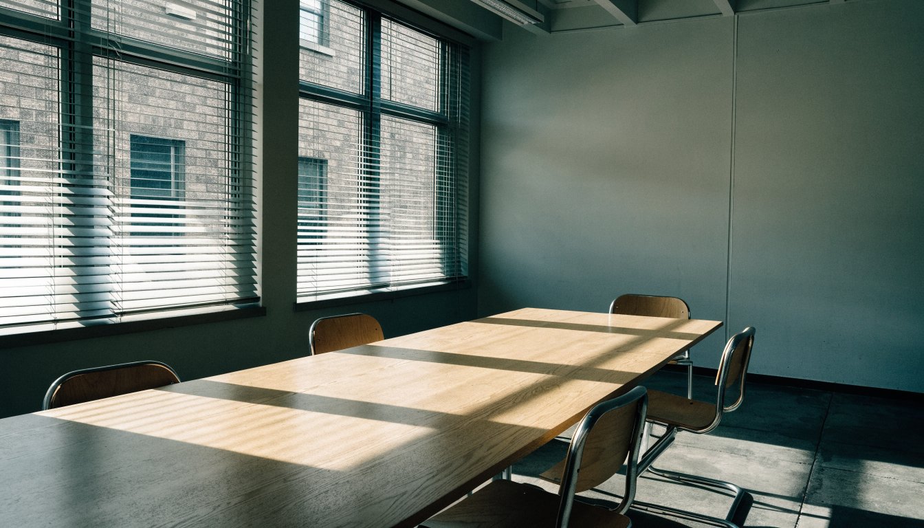 An empty meeting room with venetian blind light across a bare table, illustrating the RECO discipline process in Ontario.
