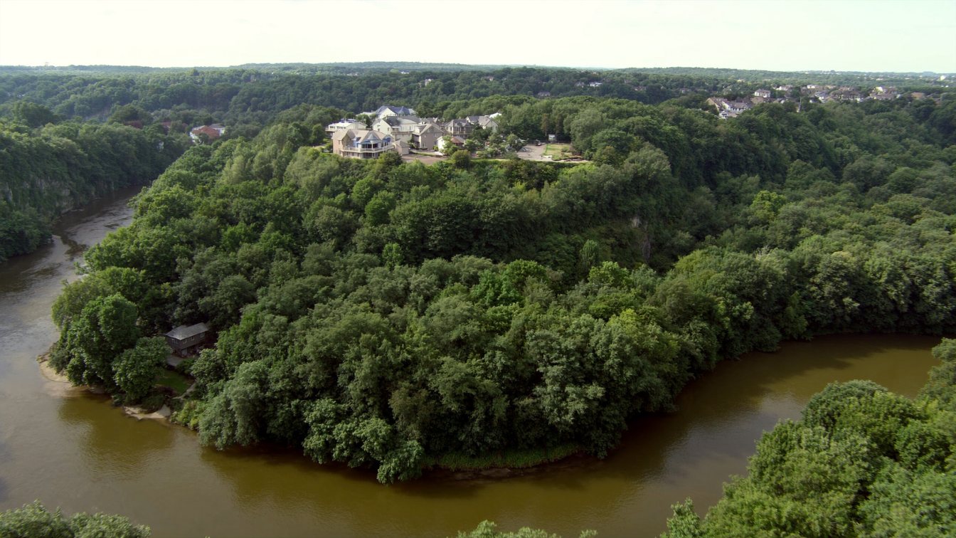 Wooded ravine with a river winding below the back gardens of large houses on the tableland above in Toronto (illustrative)