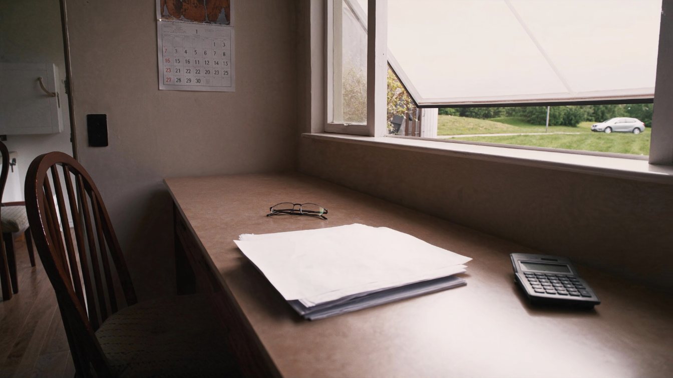 A calculator, reading glasses and a folder of papers on a kitchen table beside a window (illustrative)