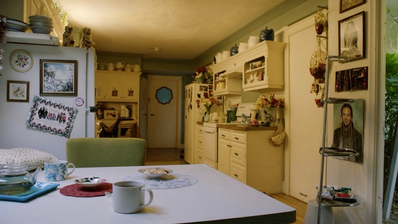An adult daughter and her father talking over coffee at a kitchen table, seen from behind (illustrative)
