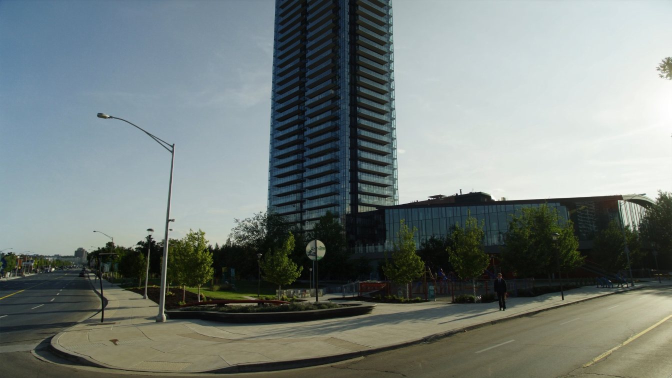 A single tall glass condominium tower beside a new urban park and subway station in a growing suburban downtown (illustrative)