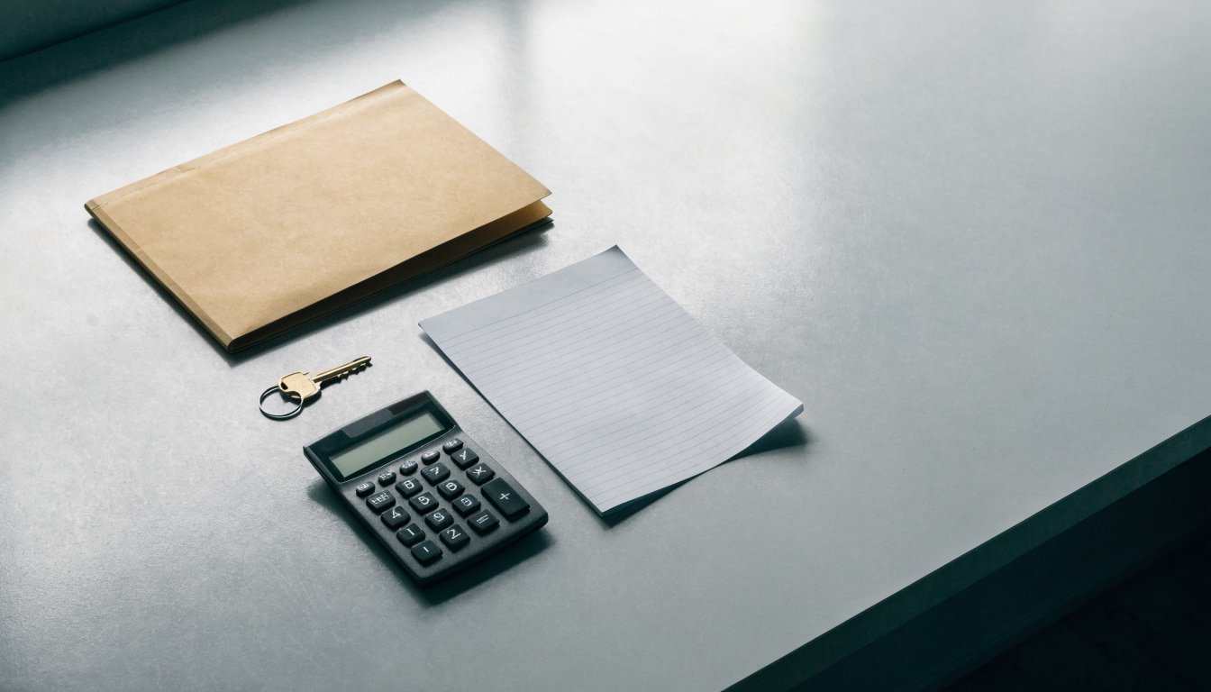A closed folder, a brass key and a calculator on a plain desk, illustrating Underused Housing Tax filing obligations.
