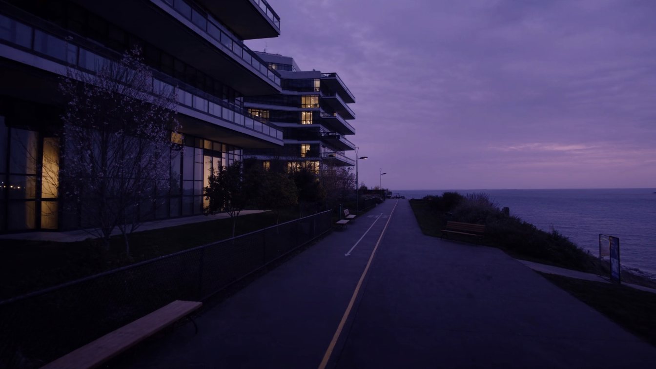 Mid-rise condominium balconies overlooking a Lake Ontario waterfront trail at dusk (illustrative)