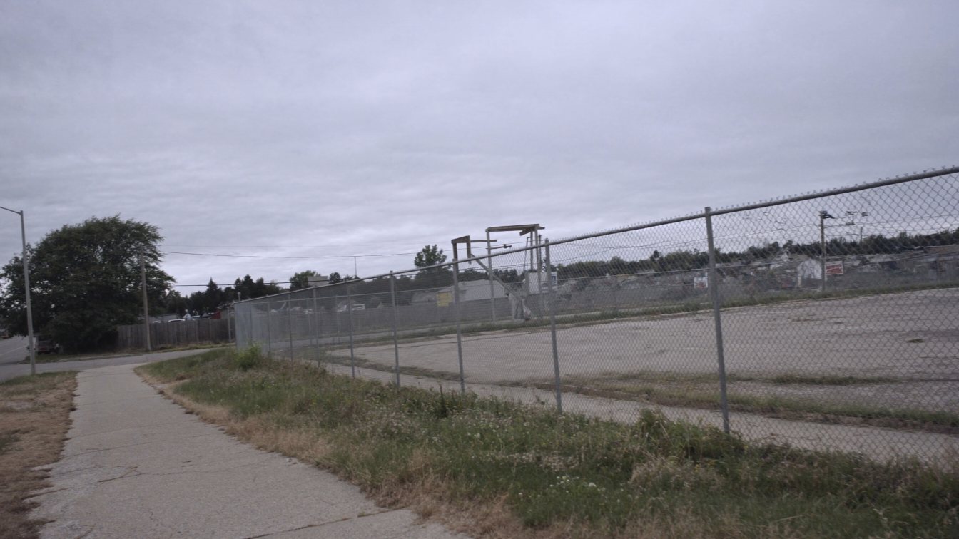 Empty fenced commercial lot on a suburban avenue (illustrative)