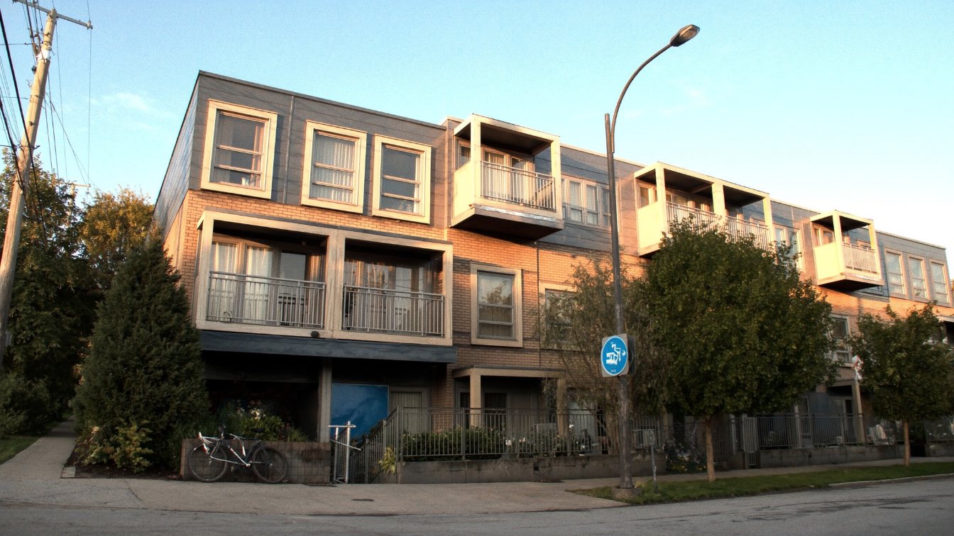 A compact mid-rise condominium building and stacked townhouses on a GTA street in the evening (illustrative)