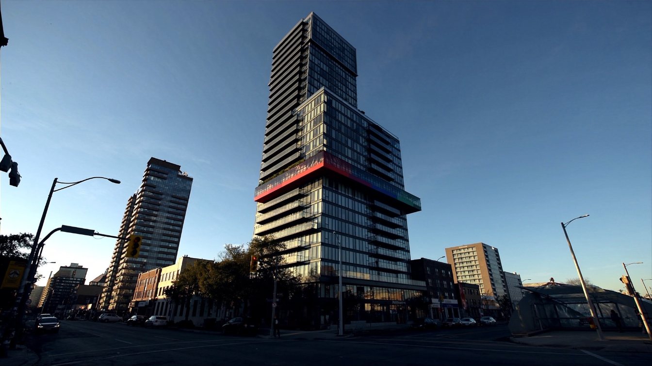 A tall glass condominium tower with a coloured band near its midpoint at a busy midtown Toronto intersection (illustrative)