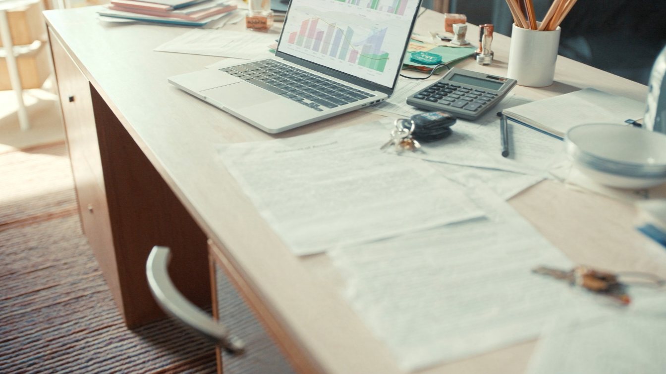 Laptop with charts, calculator and house keys on a desk (illustrative)