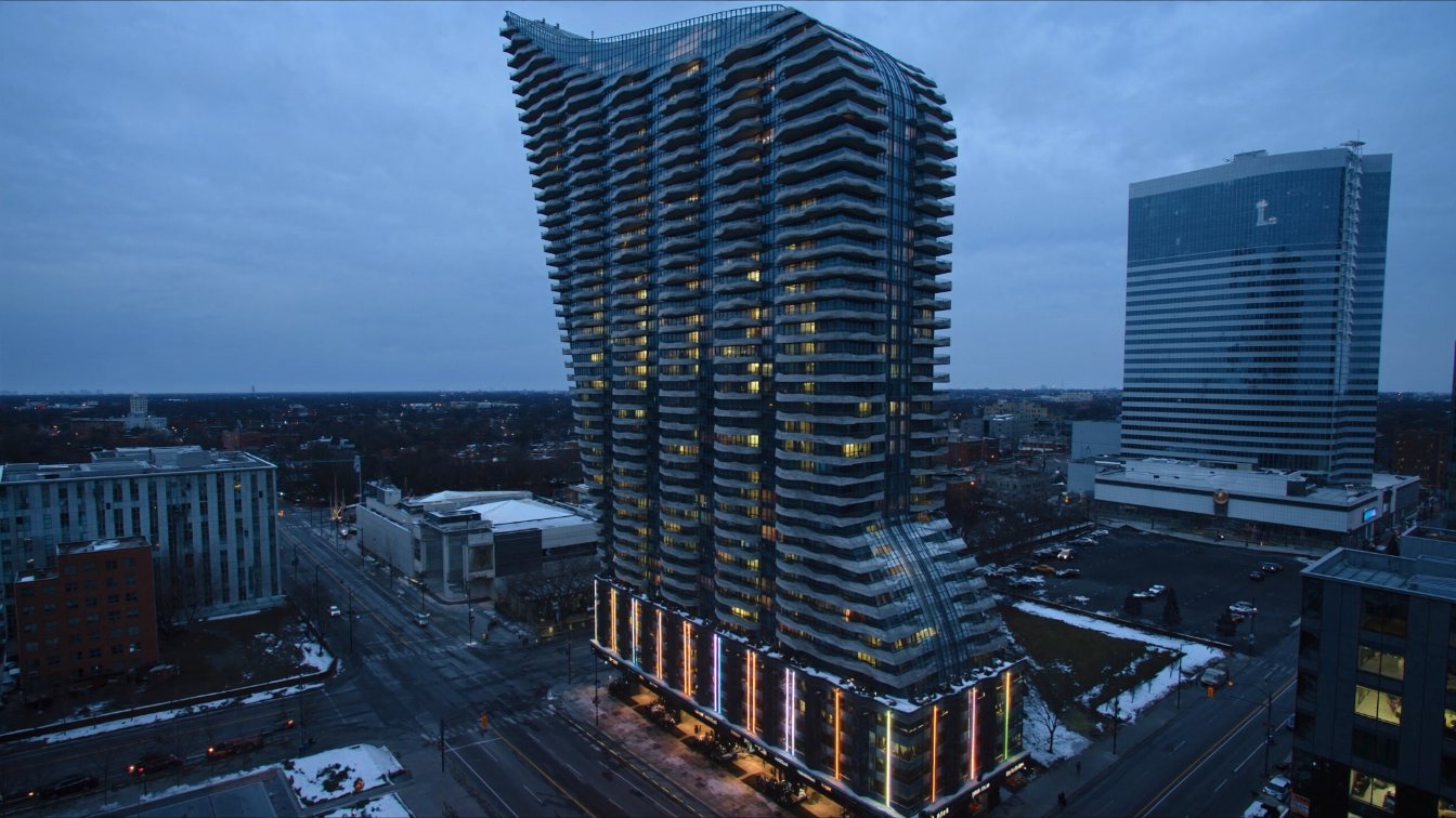 A tall glass condominium tower that curves outward at the top beside a performing arts centre in downtown Toronto (illustrative)