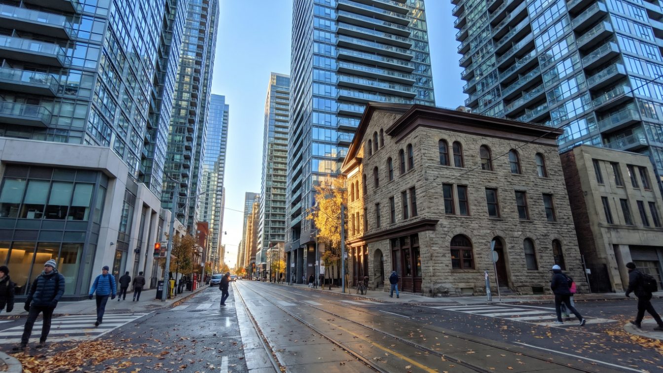 Glass condo towers beside a restored stone building on a downtown Toronto street (illustrative)