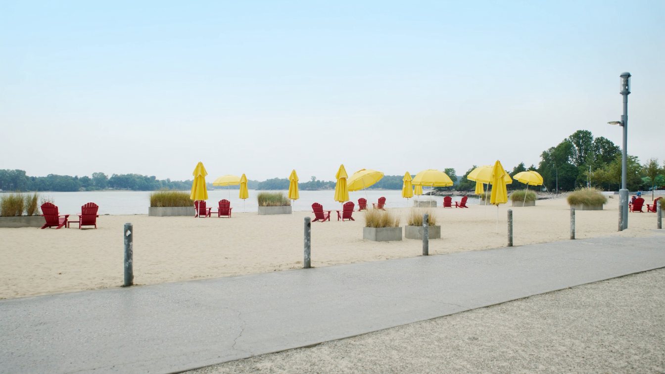 Sandy urban beach with fixed umbrellas on the Toronto waterfront, with Lake Ontario and the islands beyond (illustrative)