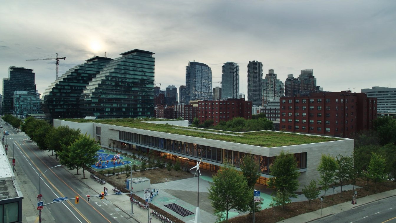 Modern school and community centre building with a green roof beside a park among downtown Toronto condominium towers (illustrative)