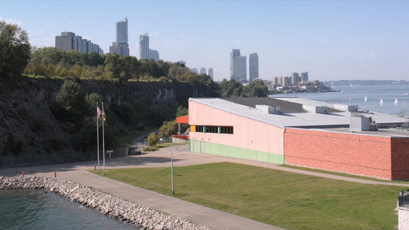 Low-rise waterfront school and community centre beside the Queens Quay promenade and lakefront condominium towers (illustrative)