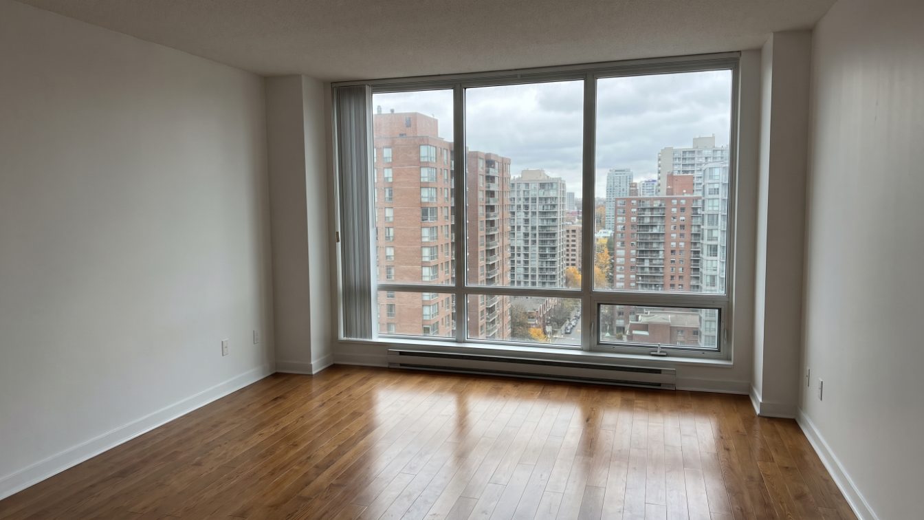 Empty condo living room with a window view of mid-rise towers on an overcast day (illustrative)